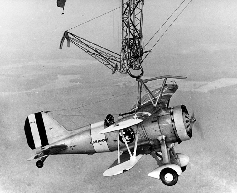 Curtis Sparrowhawk fighter hanging from the trapeze of USS Macon. Trapnell provided designs to fix serious flaws with the original trapeze system.