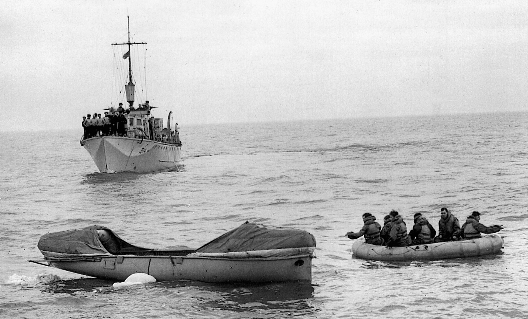 In a test maneuver, a raft filled with six men approaches a lifeboat under the watchful eyes of Navy comrades. 