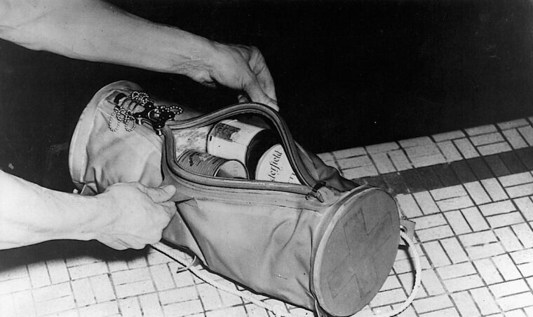 A sailor holds onto an abandon ship kit as he paddles in a pool. The buoyant kit held medical supplies, and even left room for a pack of cigarettes.