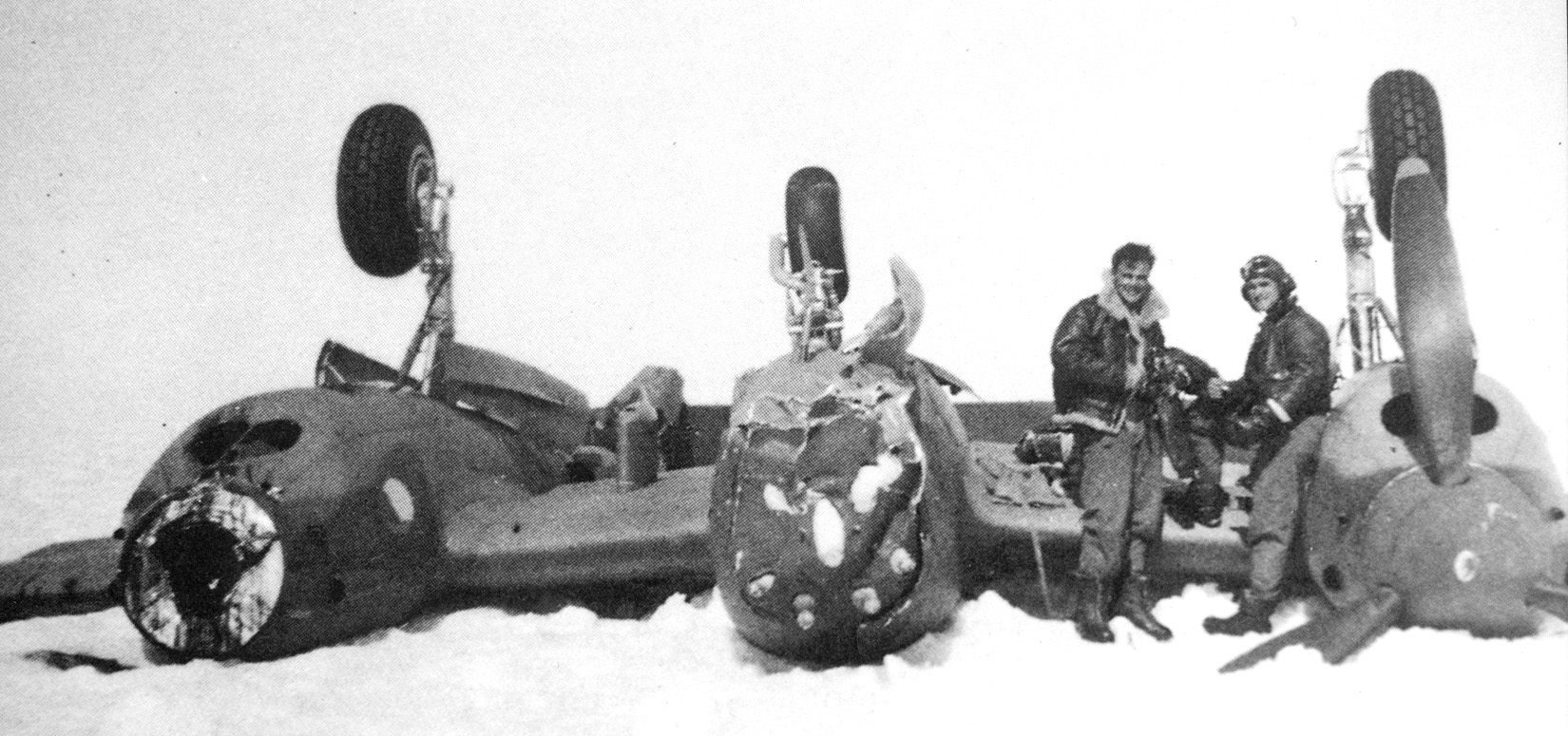 Two airmen stand alongside the P-38 piloted by Brad McManus, which flipped while rolling along the ice during its forced landing on Greenland.