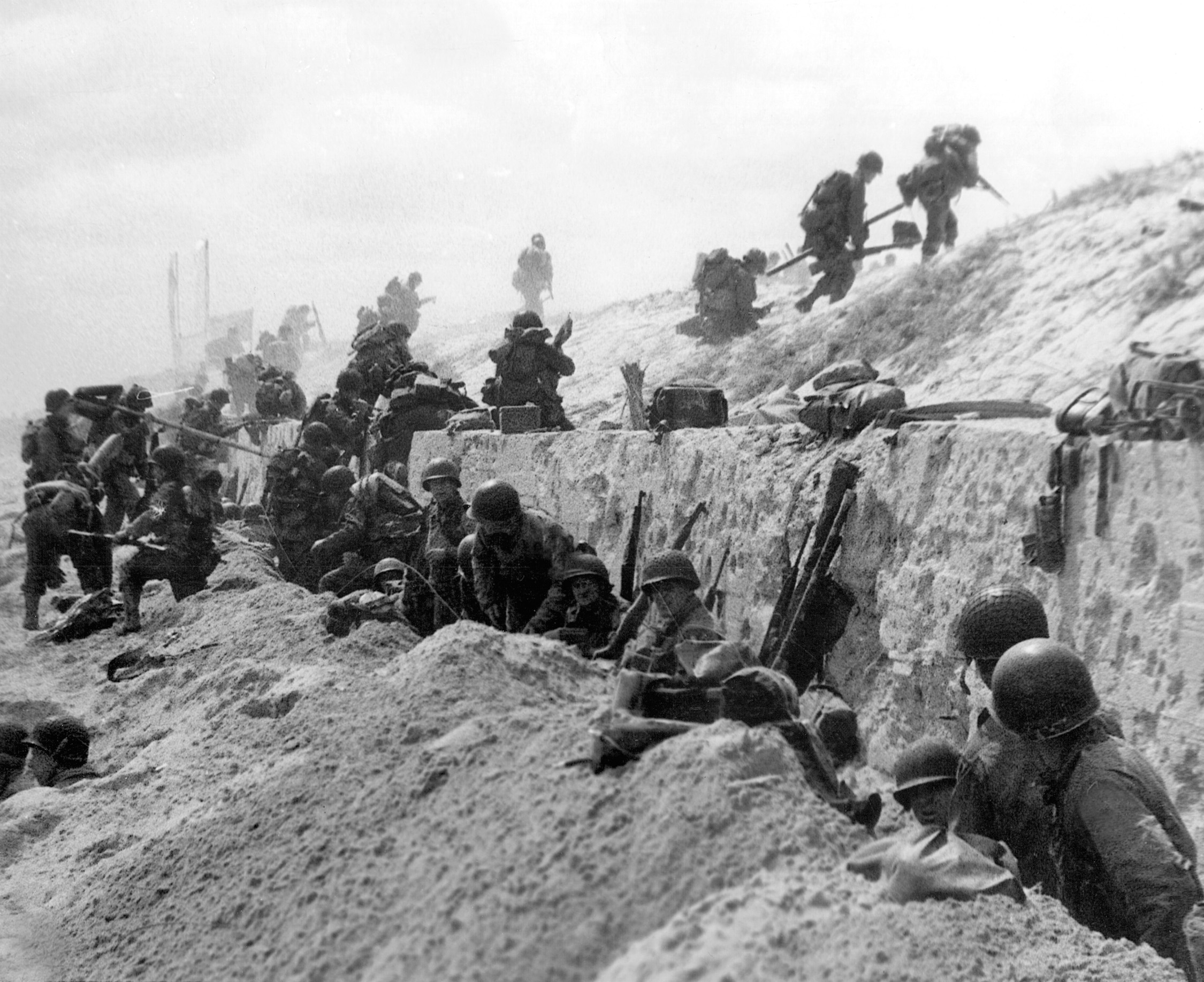After consolidating their positions on Utah Beach and catching their breaths behind the cover of a stone wall, U.S. troops begin the long trek inland on the morning of D-day.
