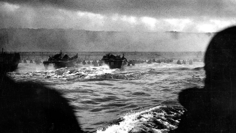 U.S. landing craft churn through the rough waters of the English Channel toward the coast of Normandy. The morning haze and the smoke ofå battle blow across the beaches, while some soldiers have already disembarked and wade the last few feet to shore.