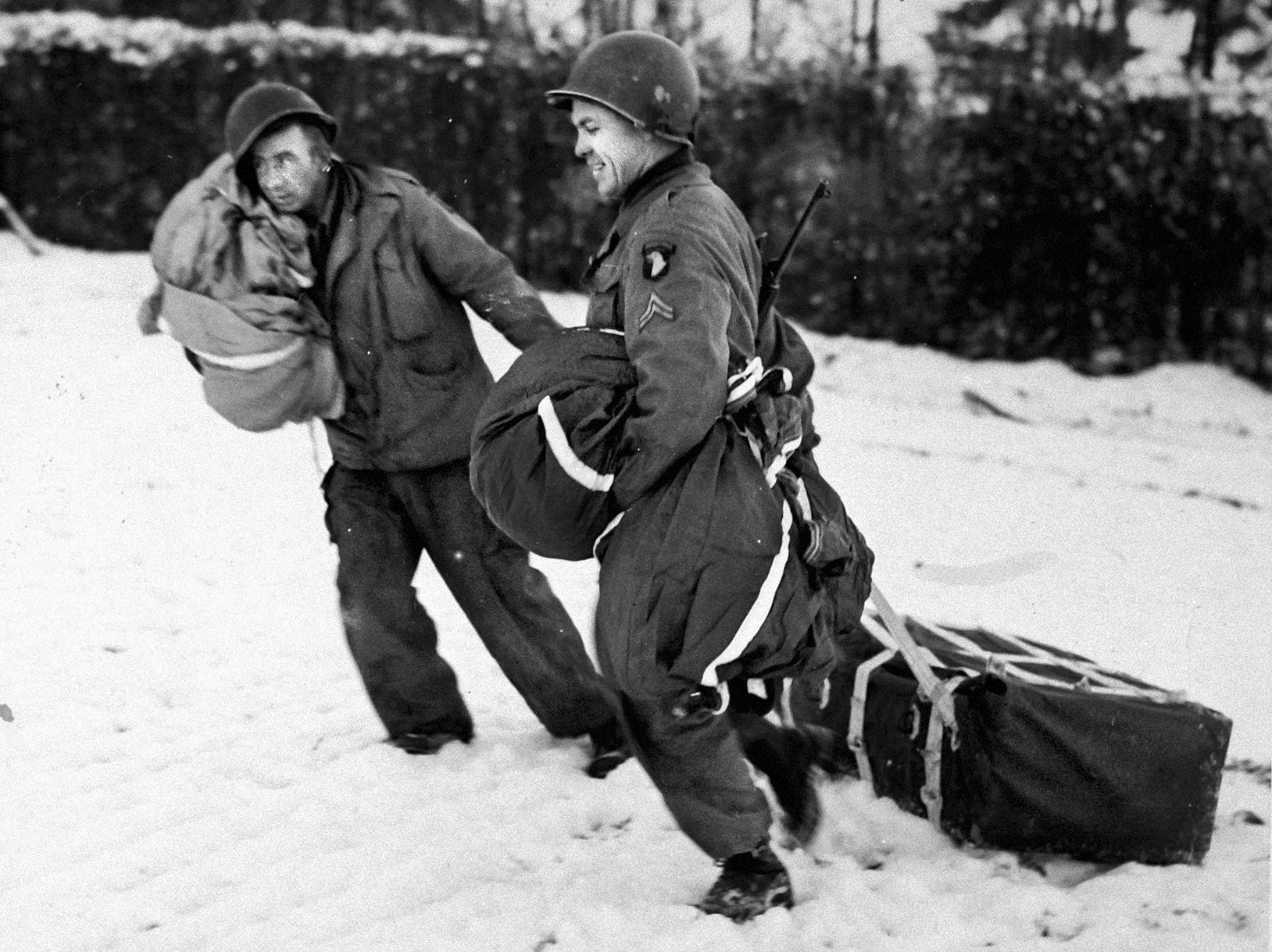 American troopers of the 101st Airborne Division drag supply containers air dropped to them during the siege of Bastogne. The 101st was surrounded at the Belgian crossroads town, and as the number of wounded increased, the losses sustained in the 326th Airborne Medical Company severely strained the ability of available medical personnel to care for those injured.