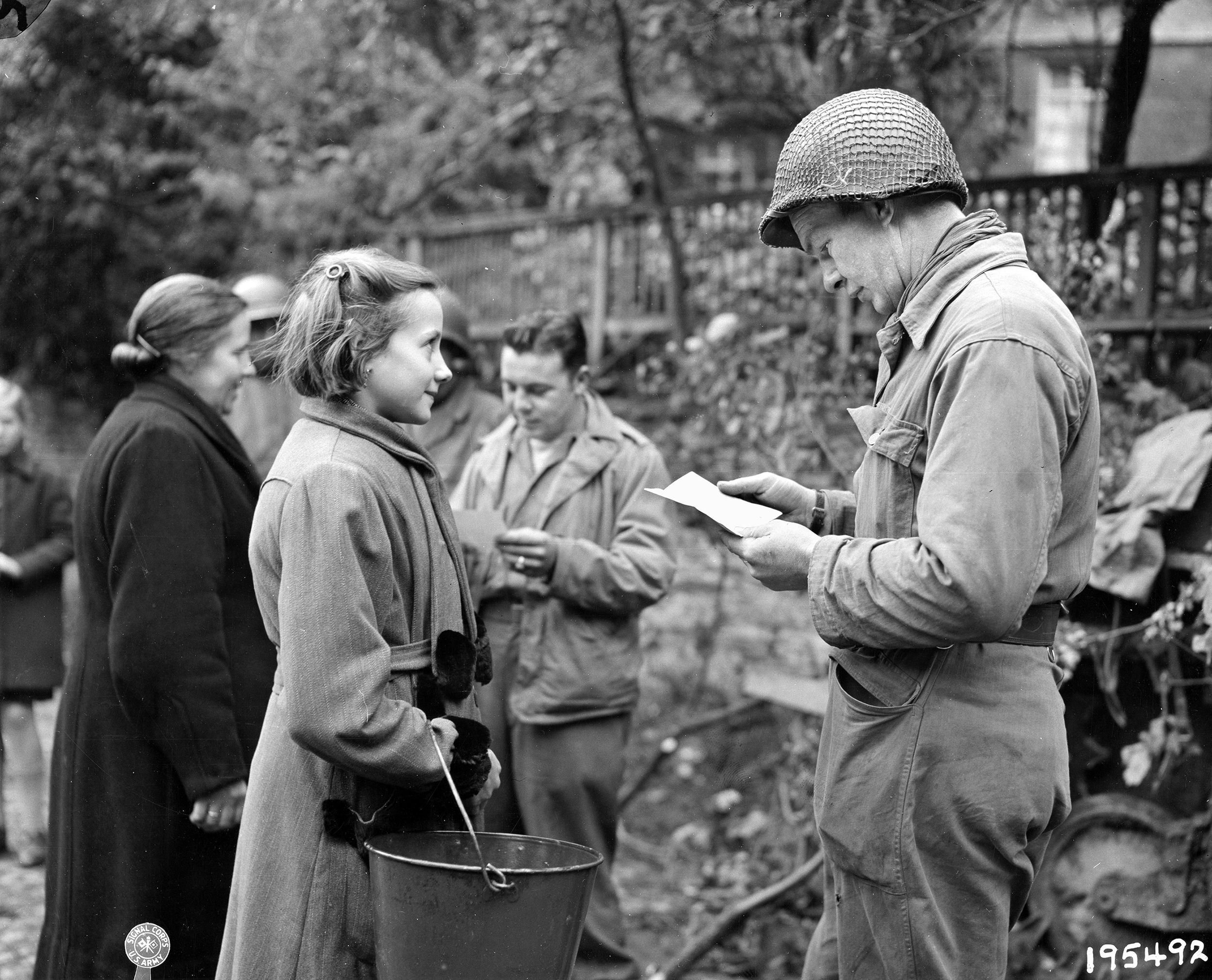 An American soldier inspects the papers of a young German girl. Cohn discovered a Dutch woman in Cologne who sheltered two girls and used her own food ration card to feed them. He was shocked to learn the girls could not get ration cards because they were Jewish.