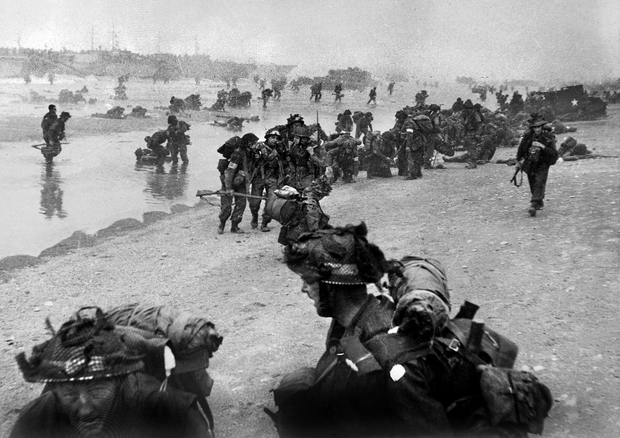 Troops from several units fight the Germans and prepare wounded for evacuation from the Queen Red sector of Sword Beach. Commandos of the 1st Special Service Brigade disembark from landing craft in the background.