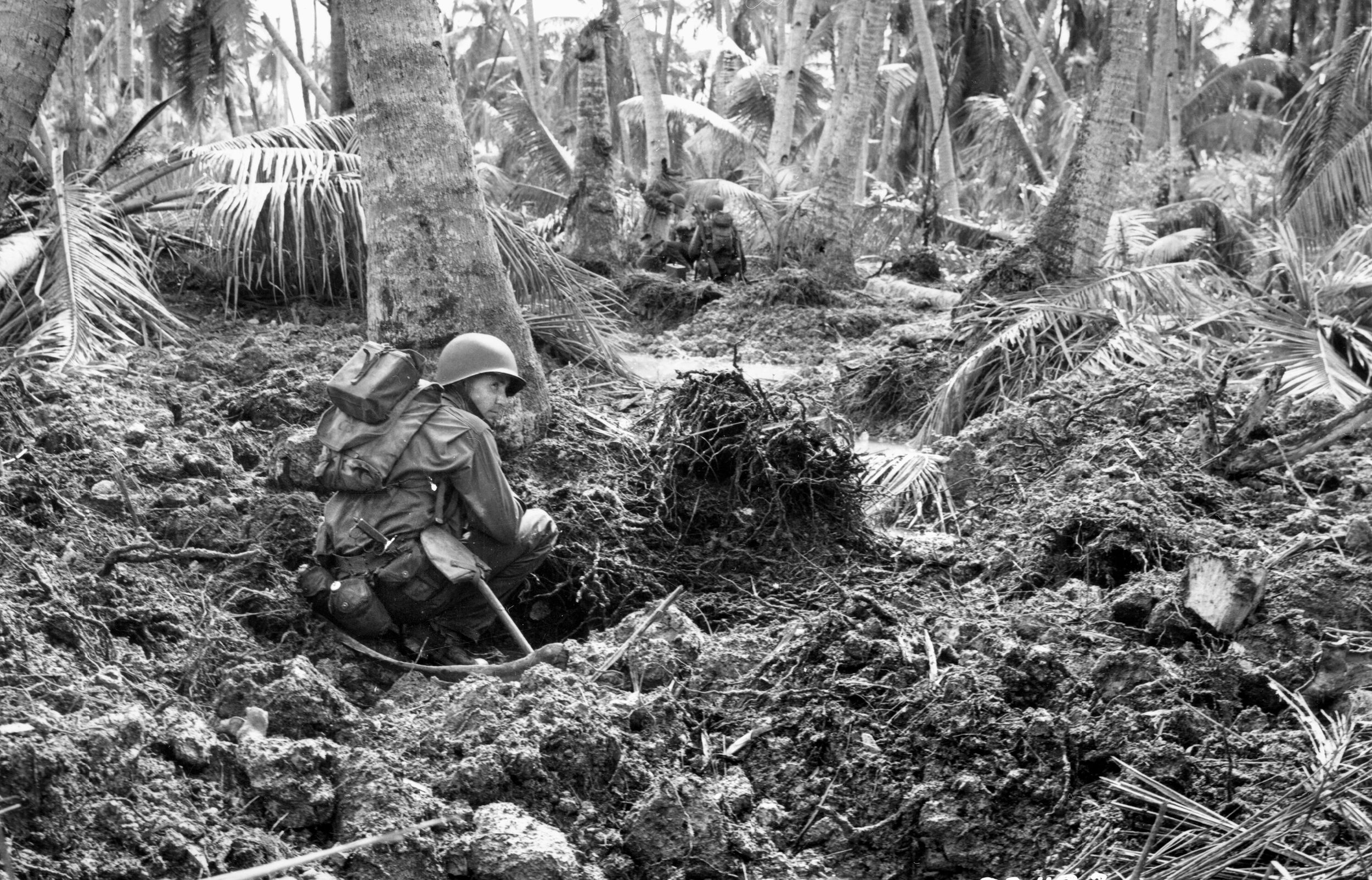 Taking cover in a shell hole, a soldier of the American 165th Infantry Regiment pauses as other troops also move forward from Red Beach at Makin, November 20, 1943.