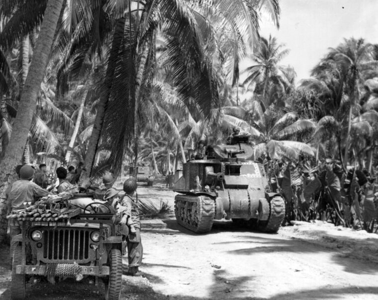 An American M3 medium tank, with a sponson-mounted 75mm gun and 37mm cannon mounted in a small turret, rolls across the sandy terrain of Butaritari. This tank belongs to the 193rd Tank Battalion, and though rapidly obsolescent the M3 outclassed any Japanese armor in the Pacific. Some of the Japanese strongpoints proved difficult for the 75mm guns to crack as the tanks accompanied the Army’s 27th Division in taking Makin.