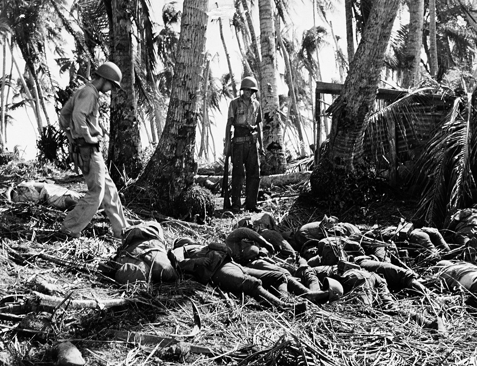 After reaching the beach at Makin, U.S. Coast Guardsmen in service with the Navy inspect the corpses of Japanese soldiers killed defending the atoll. These Coast Guardsmen were probably operating one of the landing craft that brought soldiers of the 27th Infantry Division ashore hours earlier.
