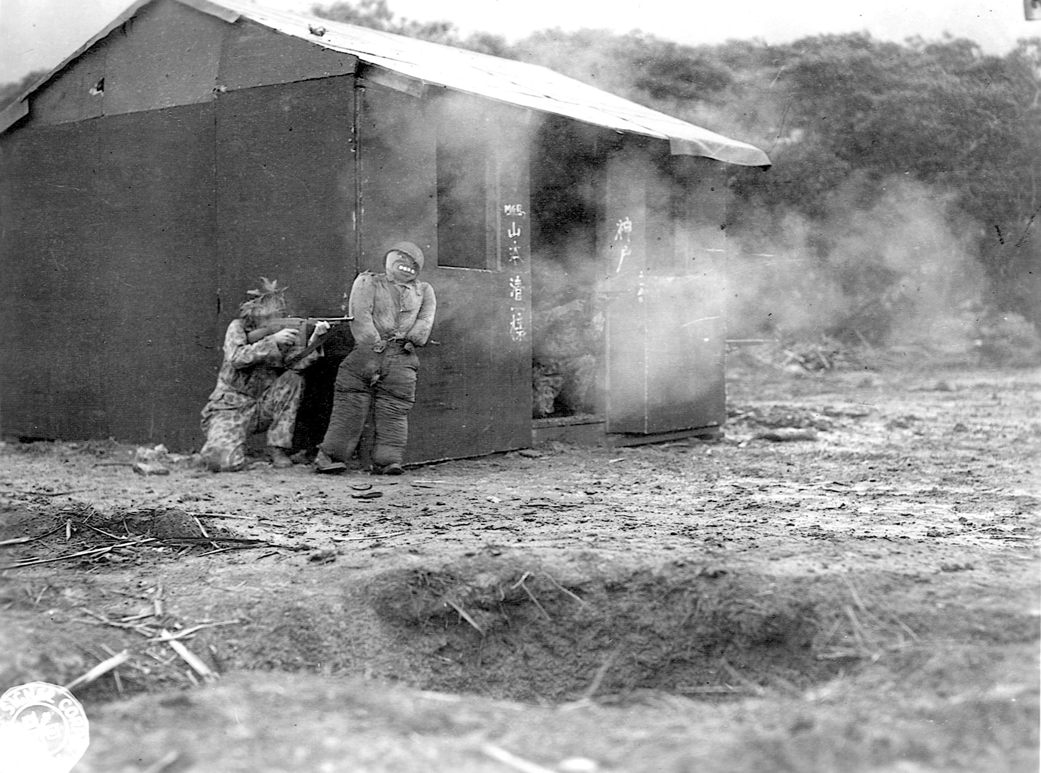 Firing Thompson submachine guns, well-camouflaged soldiers clear a street before advancing. The disarmed Japanese soldier is one of the stereotyped mockups.