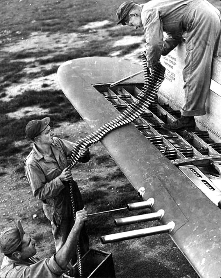 Armorers load .50 caliber ammunition belts into the four ammo trays of a P-47 Thunderbolt. 