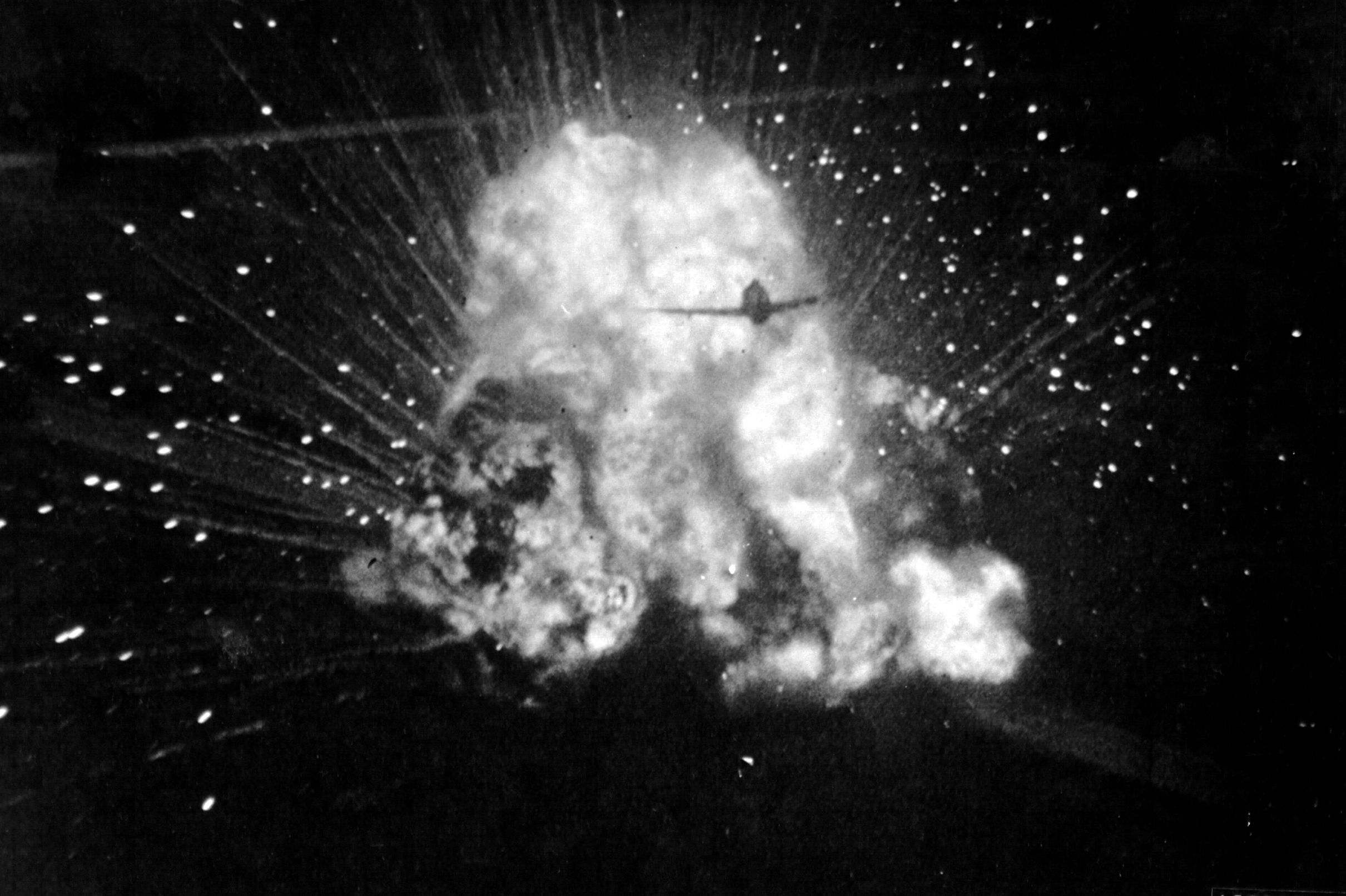 A P-47 Thunderbolt from 406th Fighter Group silhouetted against an exploding ammunition truck as the pilot strafes ground targets in France on June 23, 1944.