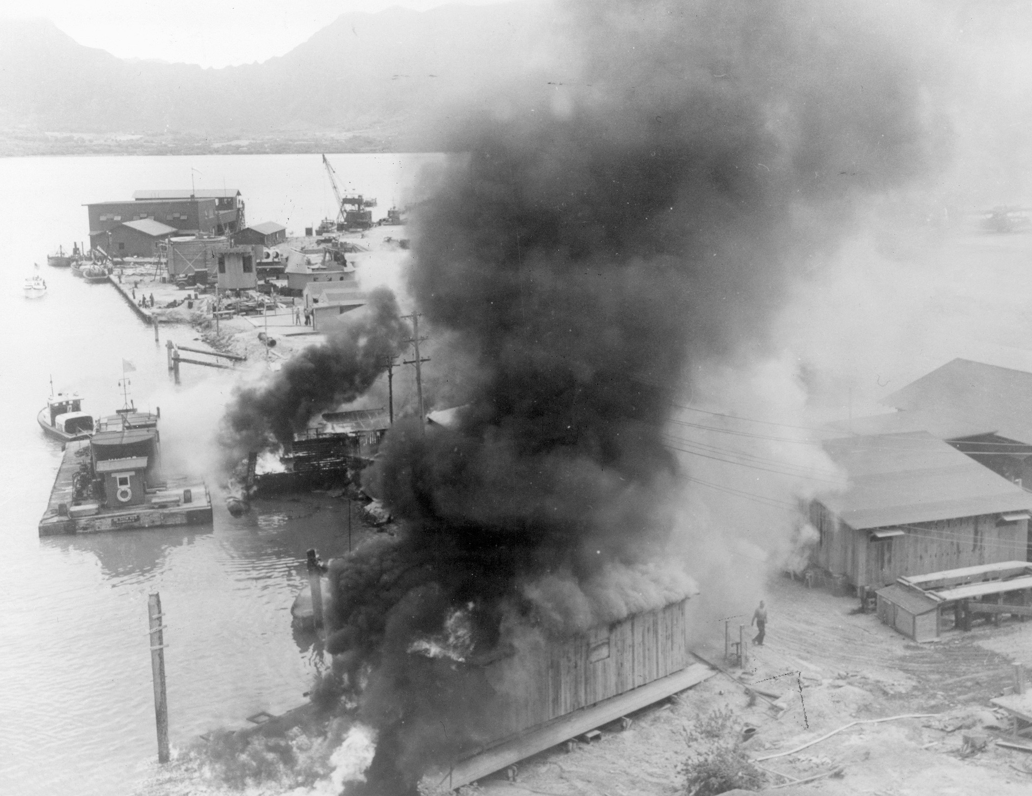 Shore installations belch smoke and flame after being bombed and strafed by Japanese aircraft. This photo of the damage at Pearl Harbor is believed to be previously unpublished.
