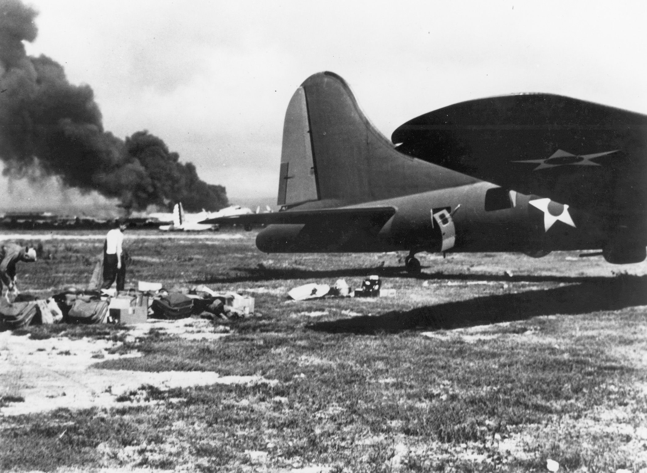 This Boeing B-17E Flying Fortress of the 7th Bombardment Group (right foreground) has just arrived to join the B-17C Flying Fortress in the background where flames burn at Hickam Army Airfield, Hawaii, during the Japanese attack.
