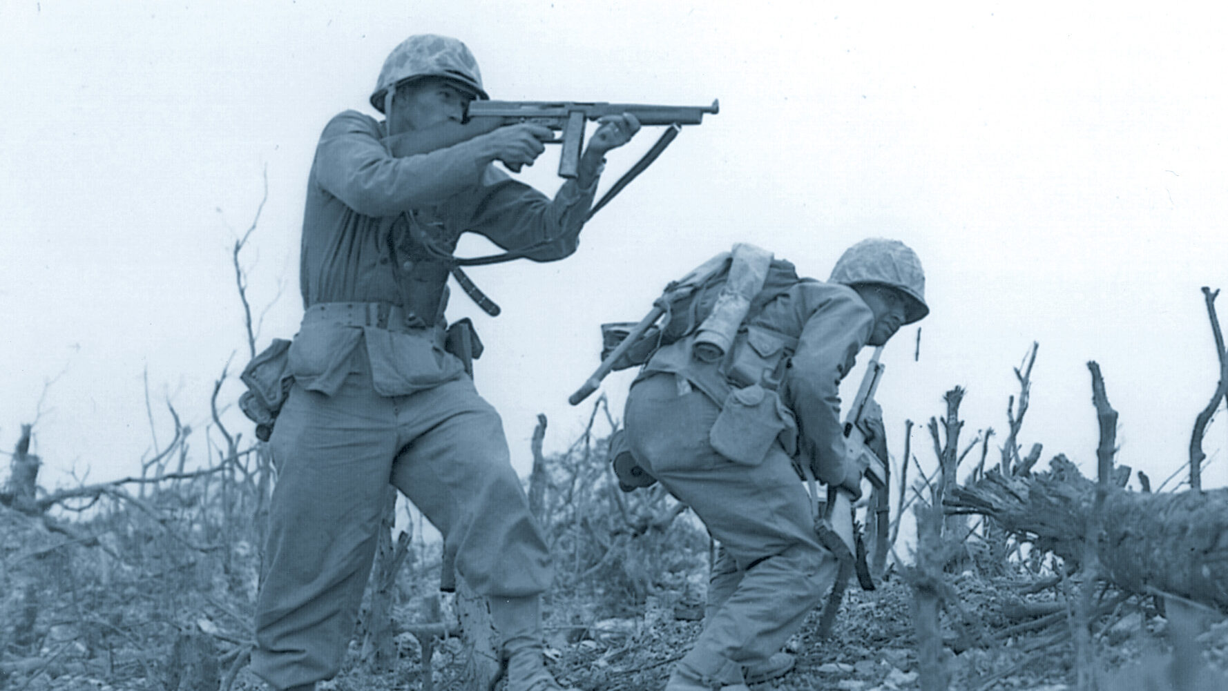 While one U.S. Marine inches forward, another fires a Tommy gun at Japanese positions on Okinawa in April 1945.