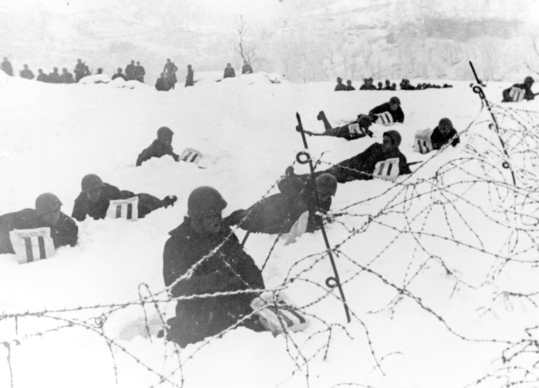 Lying in the snow, Italian soldiers are shown in defensive positions in Greece. They have just been presented with New Year’s gift packages.