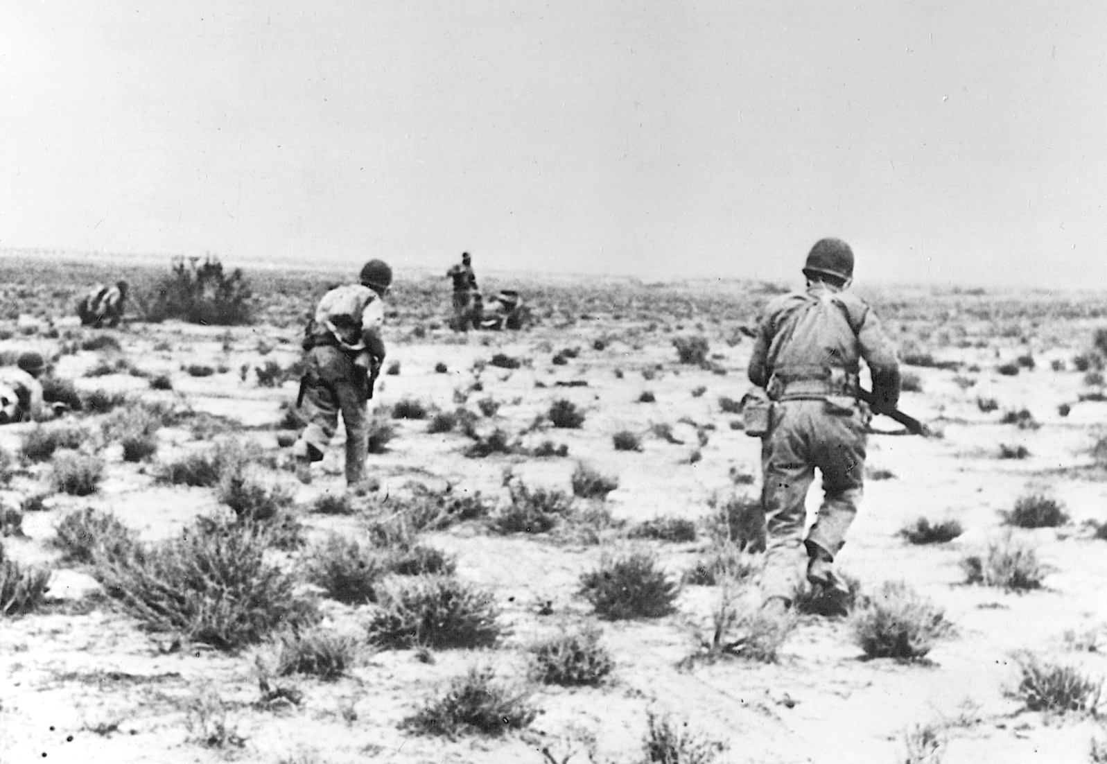 U.S. soldiers, weapons at the ready, advance warily toward German positions across the Tunisian desert.