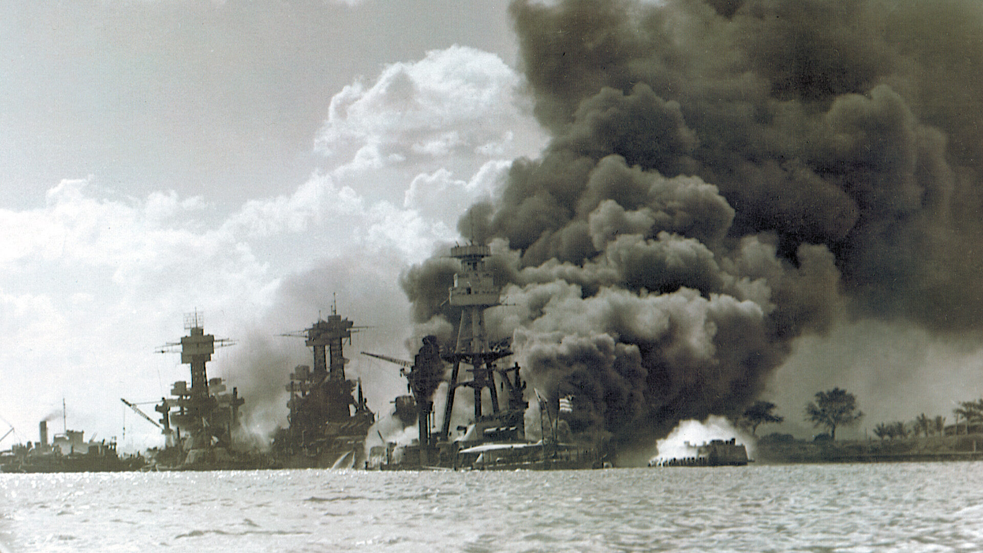 The USS West Virginia, Tennessee, and Arizona smolder and smoke in the aftermath of the surprise aerial attack by a fleet of Japanese aircraft carriers.