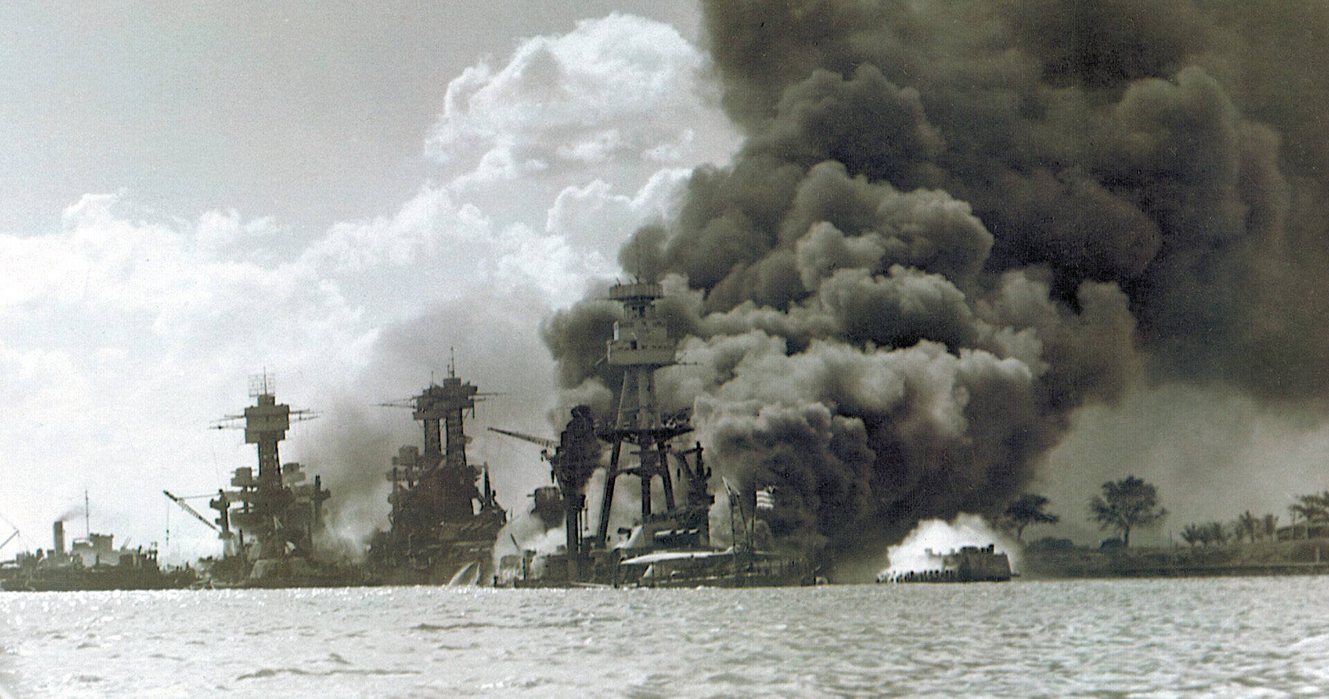 The USS West Virginia, Tennessee, and Arizona smolder and smoke in the aftermath of the surprise aerial attack by a fleet of Japanese aircraft carriers.