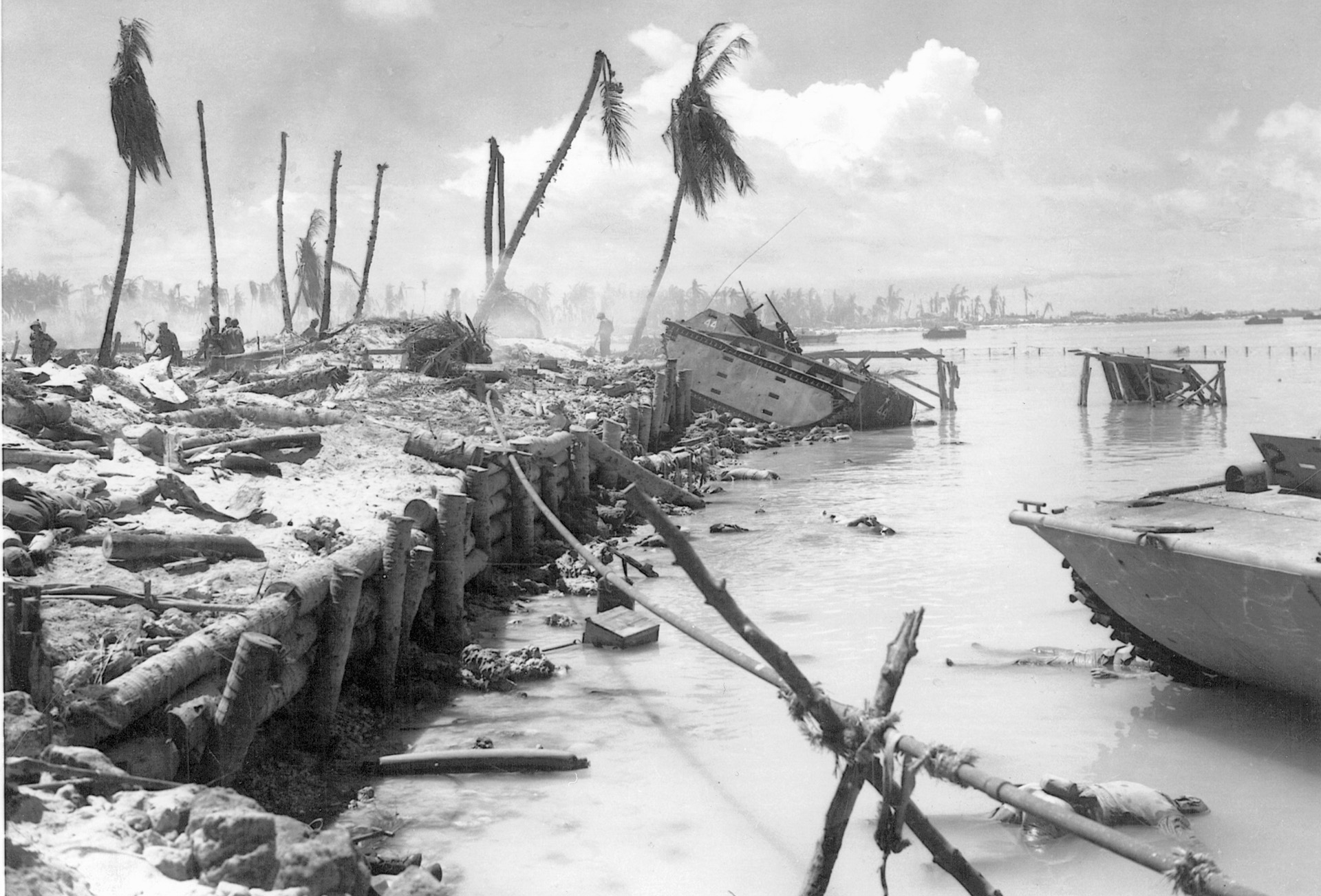 Pfc. Clayton Jay’s wrecked LVT 44 lies astride the log barrier on Red Beach 1. Other debris of war littlers the beach as the bodies of dead Marines float at the water’s edge. 