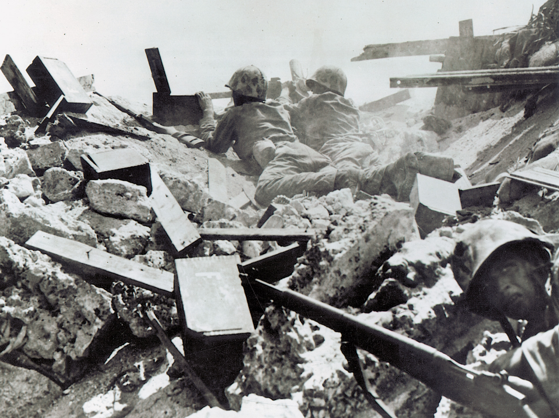 A pair of marines feverishly operates a machine gun amid the rubble of Betio while a third places his rifle to the side and crawls forward to their aid.