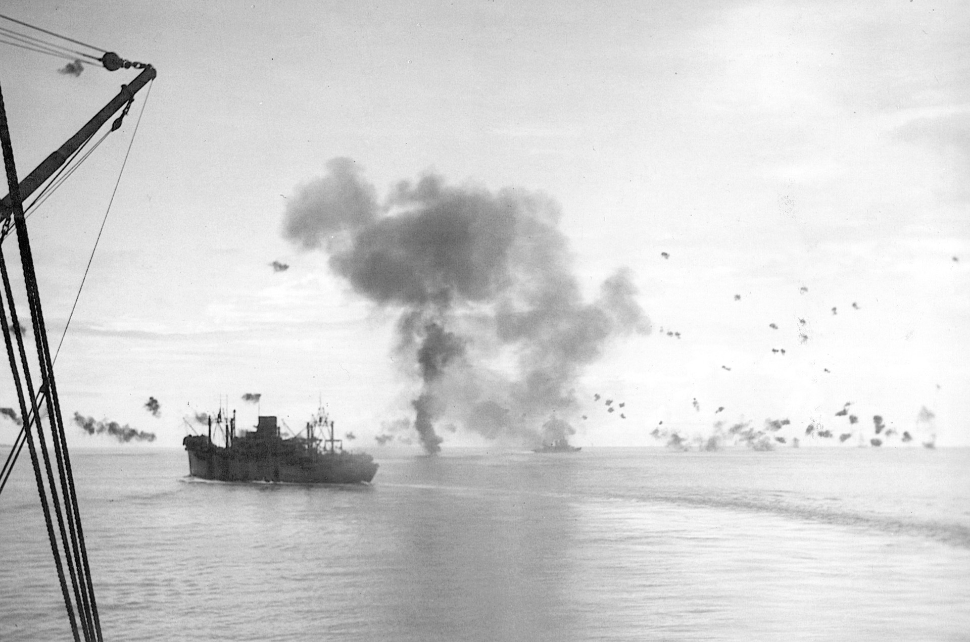 The USS President Jackson turns hard to port while in the distance the USS San Francisco burns from damage inflicted by a suicidal Betty bomber.