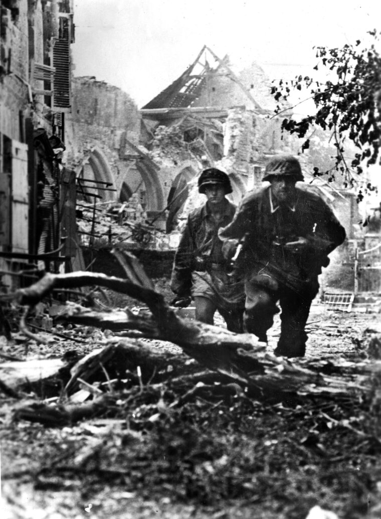 With the ruins of the Church of Saint-Pierre in the background, a pair of German panzergrenadiers pick their way through a rubble-strewn area of Caen.