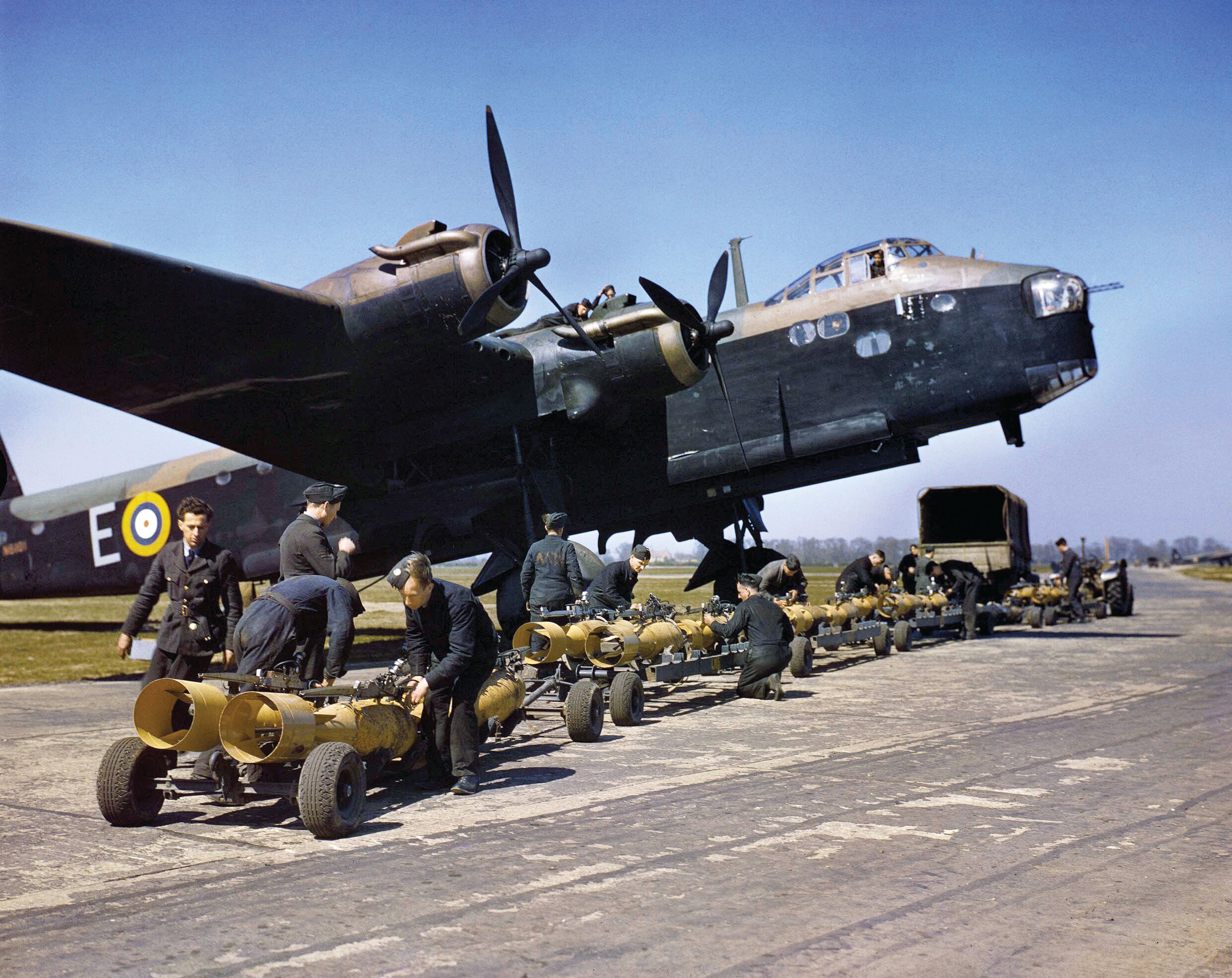 A four-engine Short Stirling bomber sits at an airfield in England while armorers prepare to place the first of 16 250-pound bombs aboard the aircraft for an RAF raid against the Third Reich.