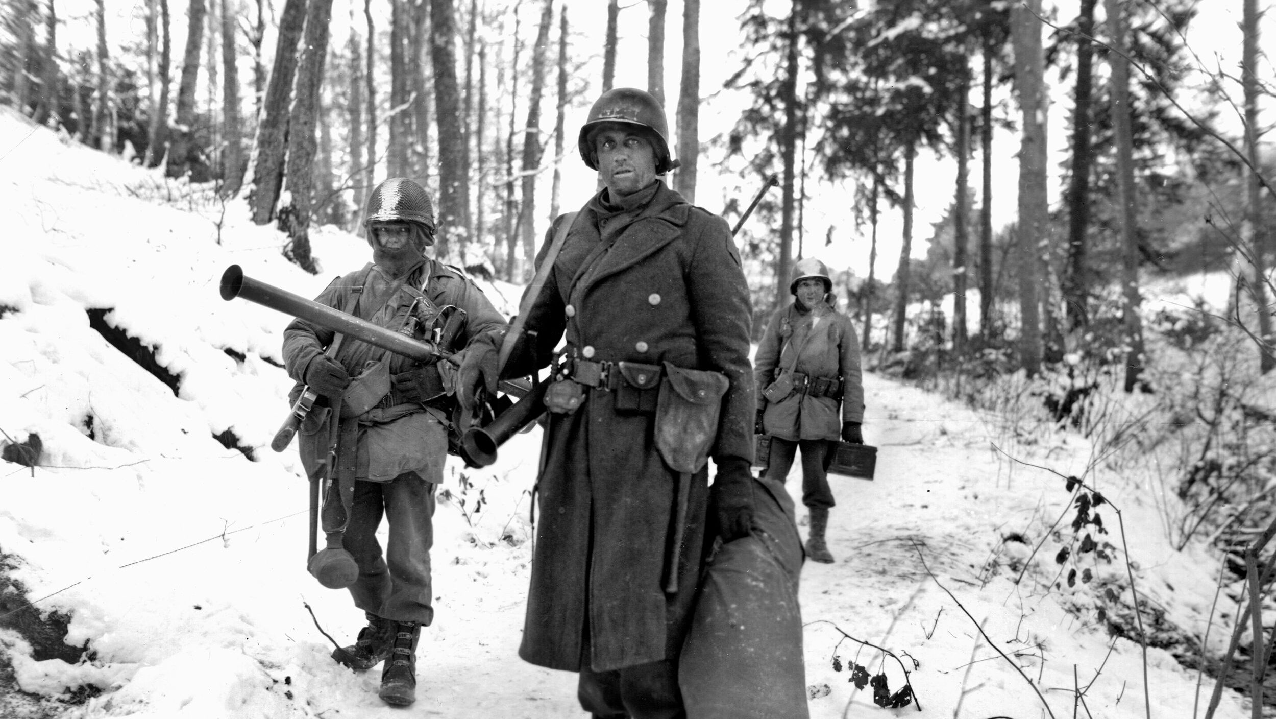 Soldiers of the 291st Engineer Combat Battalion trudge through snow while carrying bazookas. According to their commanding officer, Lt. Col. David E. Pergrin, the brave engineers stayed to defend Trois-Ponts during the Battle of the Bulge after they had been taunted by fellow soldiers. Pergrin recalled that the infantrymen had shouted, “You engineer so-and-so! Why don't you come on up there and fight?”