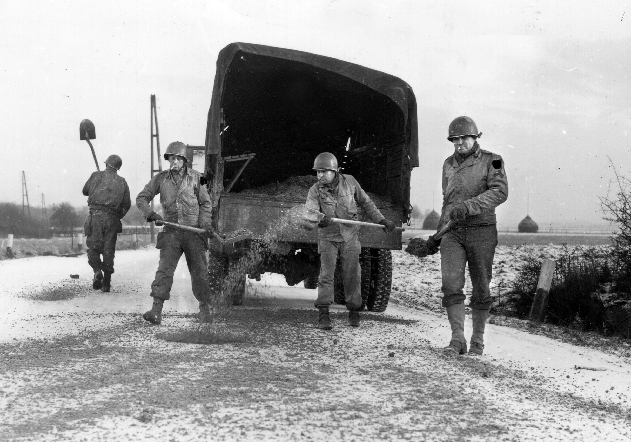 U.S. Army combat engineers shovel cinders onto an icy road in Belgium during the Battle of the Bulge. This effort was essential in moving Allied troops forward in response to the German thrust through the Ardennes Forest during December, 1944, into January, 1945.
