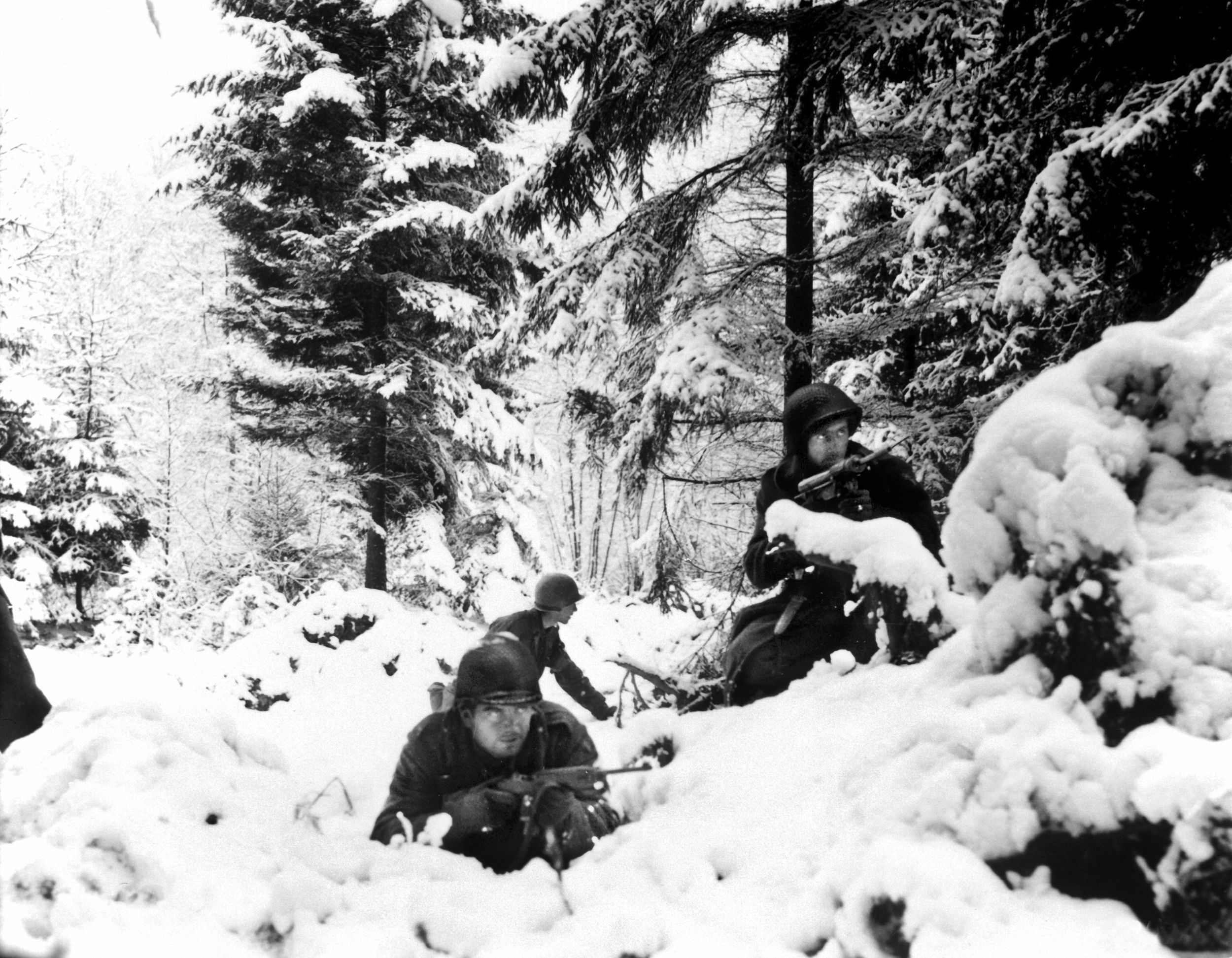 American soldiers advance warily through heavy snow during the Battle of the Bulge. The surprise German offensive caught the Americans off guard, and many service personnel were pressed into action against the enemy. Clerks, cooks, and drivers were among those who took up weapons such as the M-1 carbine in the hands of the soldier in the foreground. In fact, the carbine may indicate that this soldier has been pulled from a service post for combat duty.