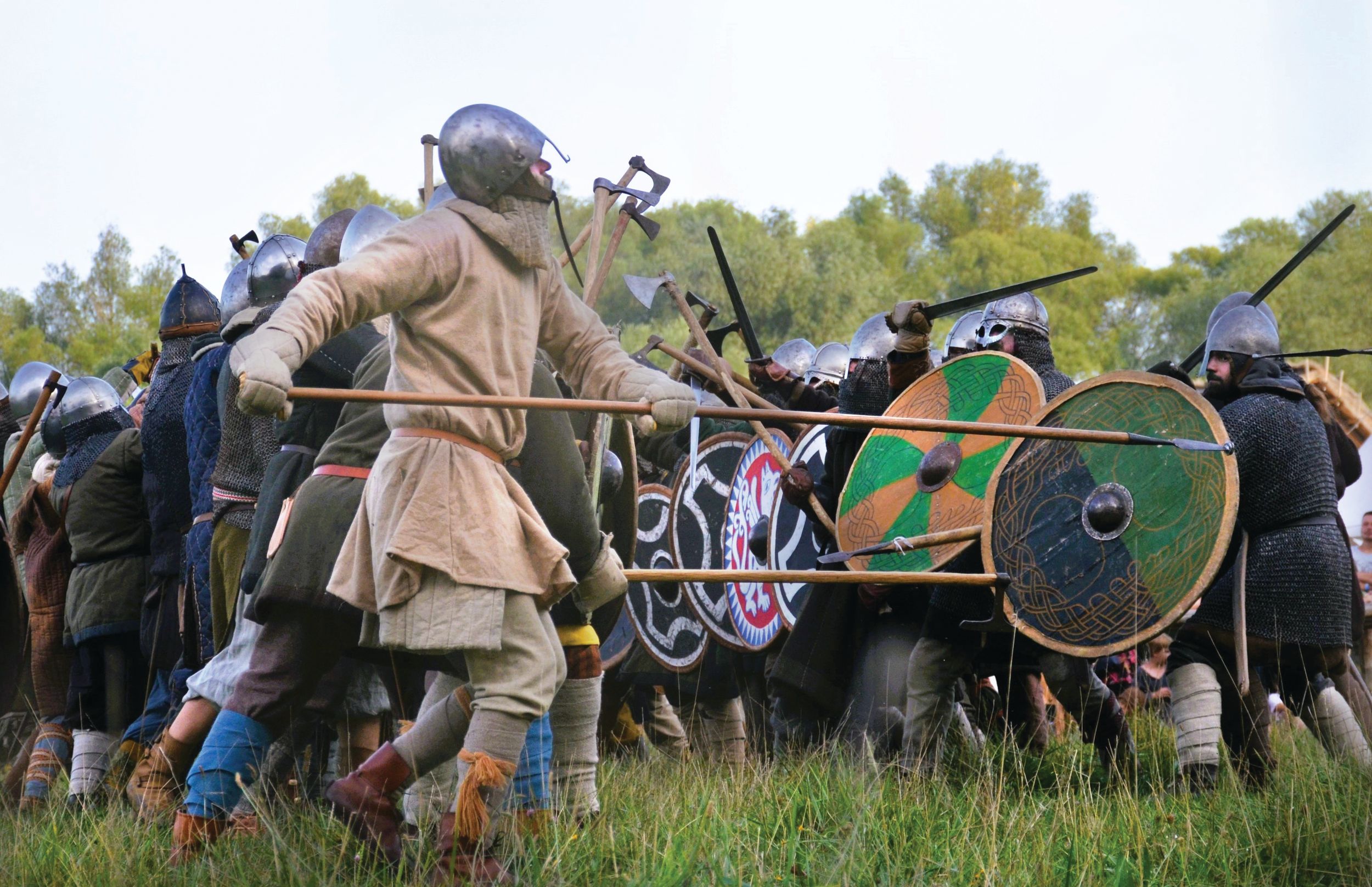 Modern European reenactors portraying Saxons and Vikings, demonstrate shield-wall combat using axes, swords, and pikes.