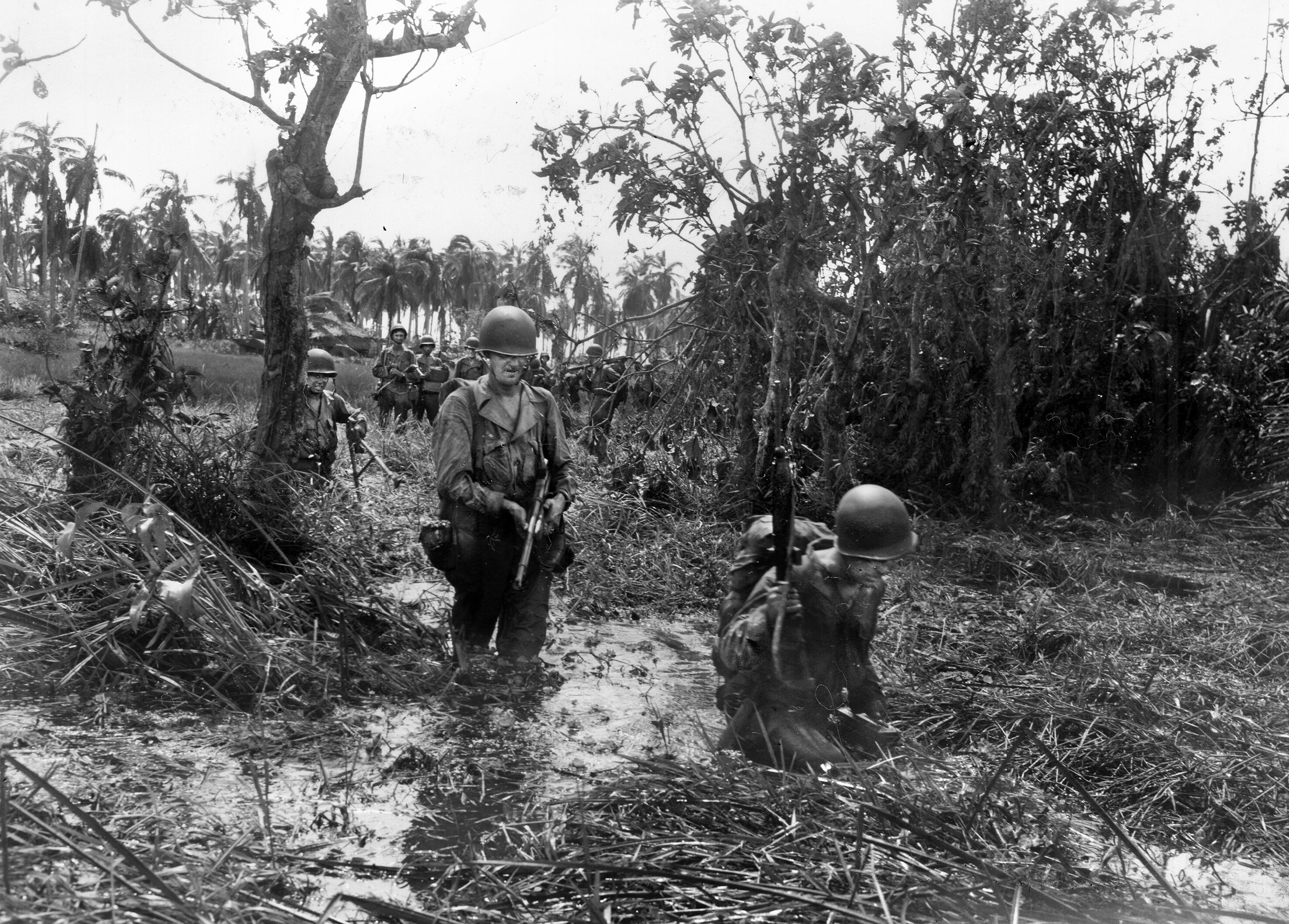 Having landed and fought their way up the beach, soldiers from the 7th Regiment (1st Cavalry Division) wade through a swamp as they head for their objective, the village of San Jose in October, 1944.