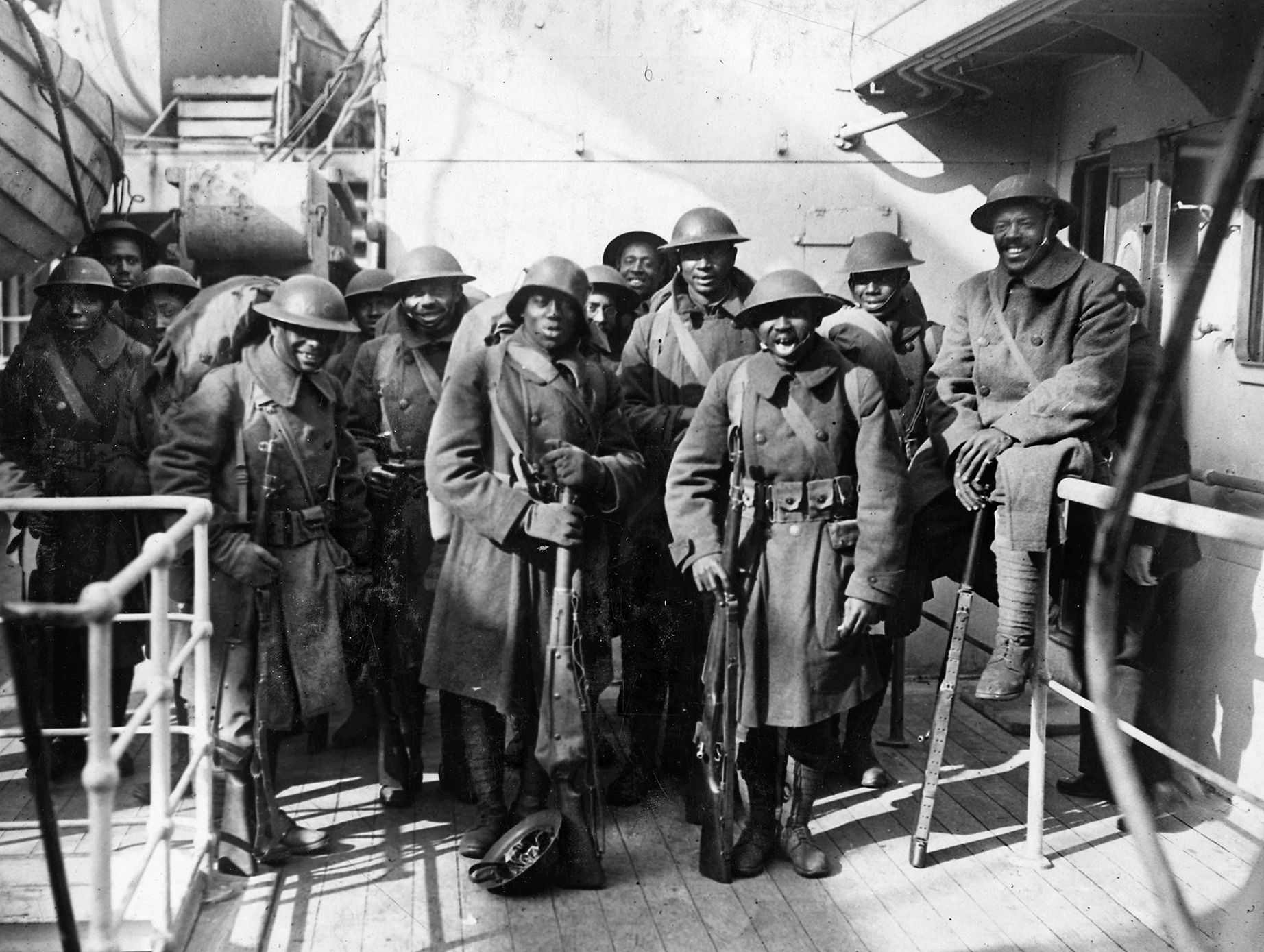 Soldiers of the 369th appear happy to be arriving at Hoboken, New Jersey after their service in France. One soldier poses with a German helmet, apparently a war trophy.