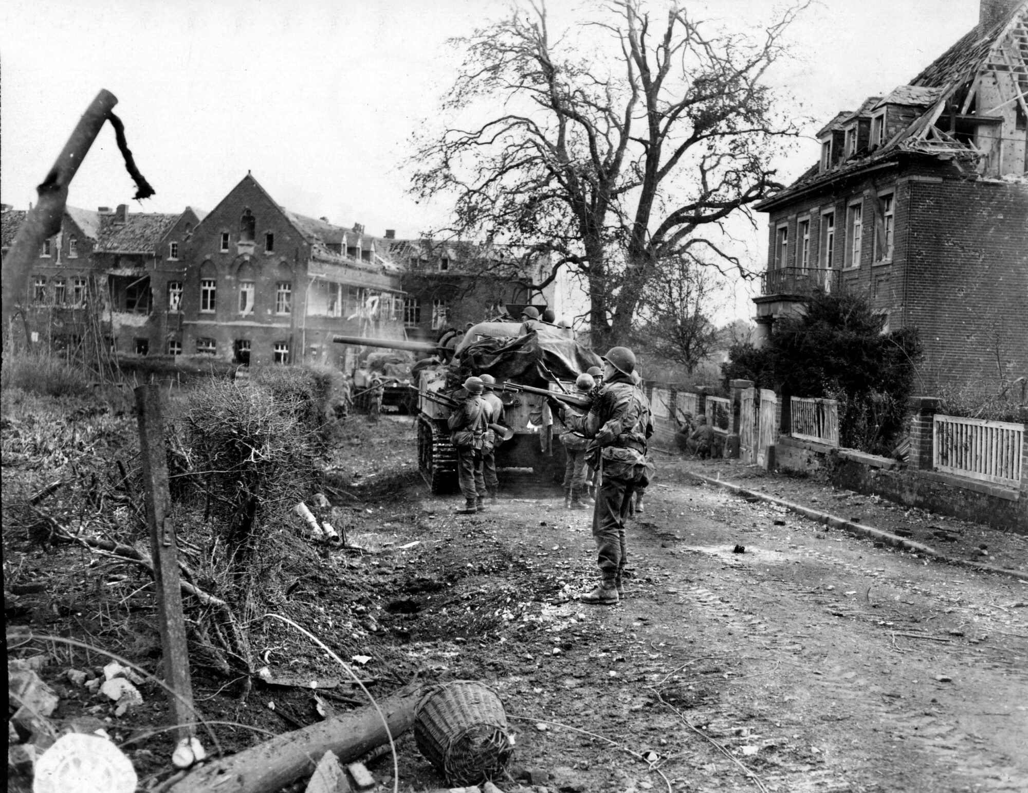 Infantrymen of the 84th Division join with machine gunners aboard Sherman tanks to concentrate fire on a German sniper holed up in Geilenkirchen. The fight for the German village lasted for more than three days.