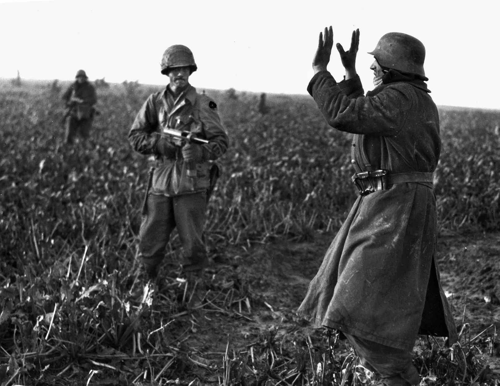 An infantryman of the 84th points his M3 submachine gun, popularly known as a “grease gun,” at a German soldier who has just thrown up his hands in surrender during the fight for Beeck, Germany. 