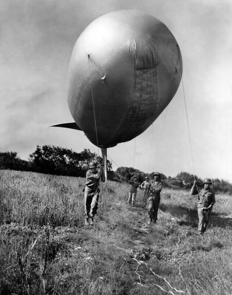 Soldiers of the U.S. Army’s 320th Barrage Balloon Battalion guide one of their balloons through a partially cleared minefield to a location off Omaha Beach. The African-American unit rendered valuable service after coming ashore at Normandy on D-Day.