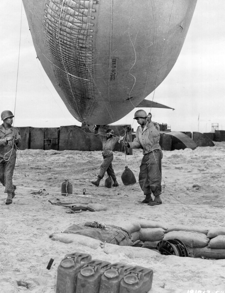 Corporal A. Johnson, of Houston, Texas, works with another soldier of the 320th Barrage Balloon Battalion to move a balloon into position with a winch on Omaha Beach. The men of the 320th came ashore under fire on D-Day at Utah and Omaha Beaches. 