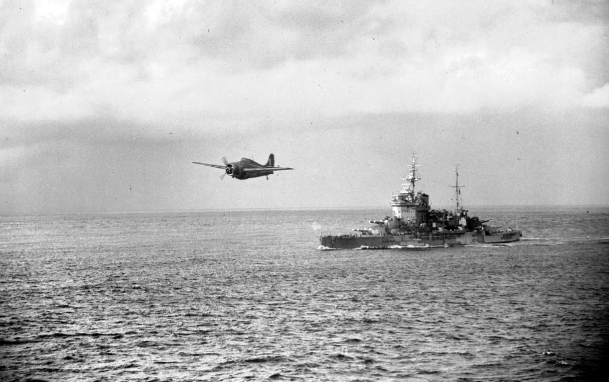 A Grumman F4F Wildcat, known as a Martlet in service with Britain’s Fleet Air Arm, flies past Warspite as it prepares to land on the British aircraft carrier Formidable during the Battle of Madagascar, March 1942. 