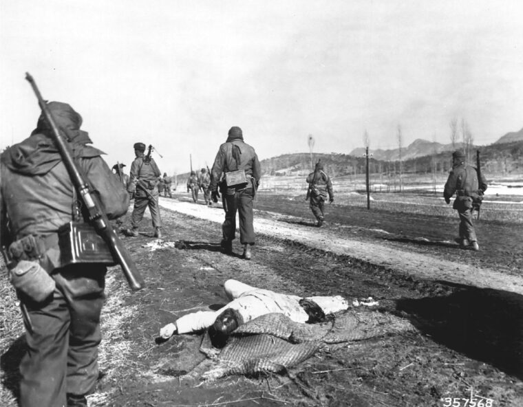 This photo, taken south of Seoul, Korea, on the day before Capt. Lewis Millett led his famous bayonet charge, shows soldiers from the 27th Infantry Regiment moving past a dead communist soldier.