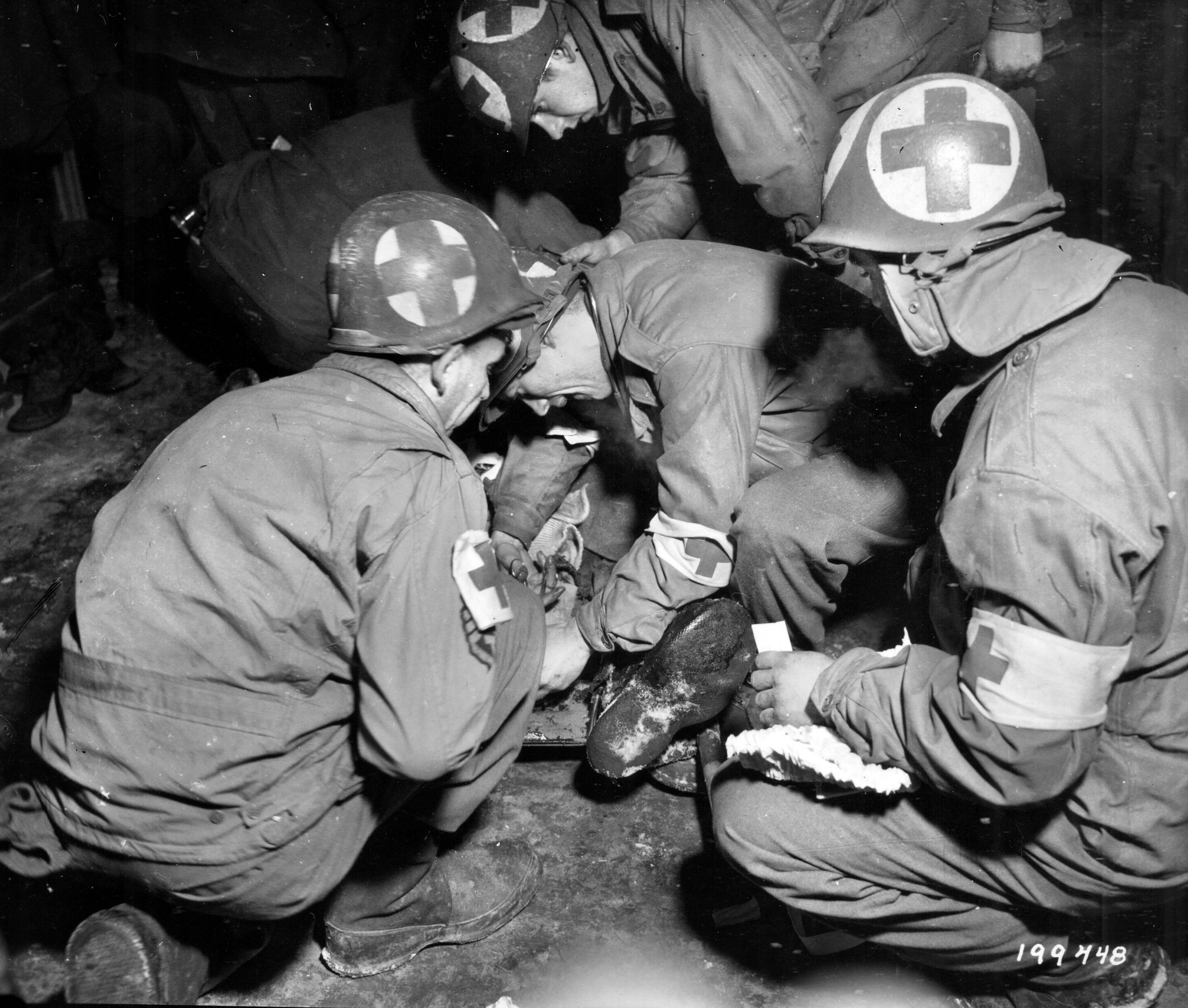 A group of medics around a seriously wounded soldier perform an emergency foot amputation. Medics saved many lives on and near the battlefield during World War II.