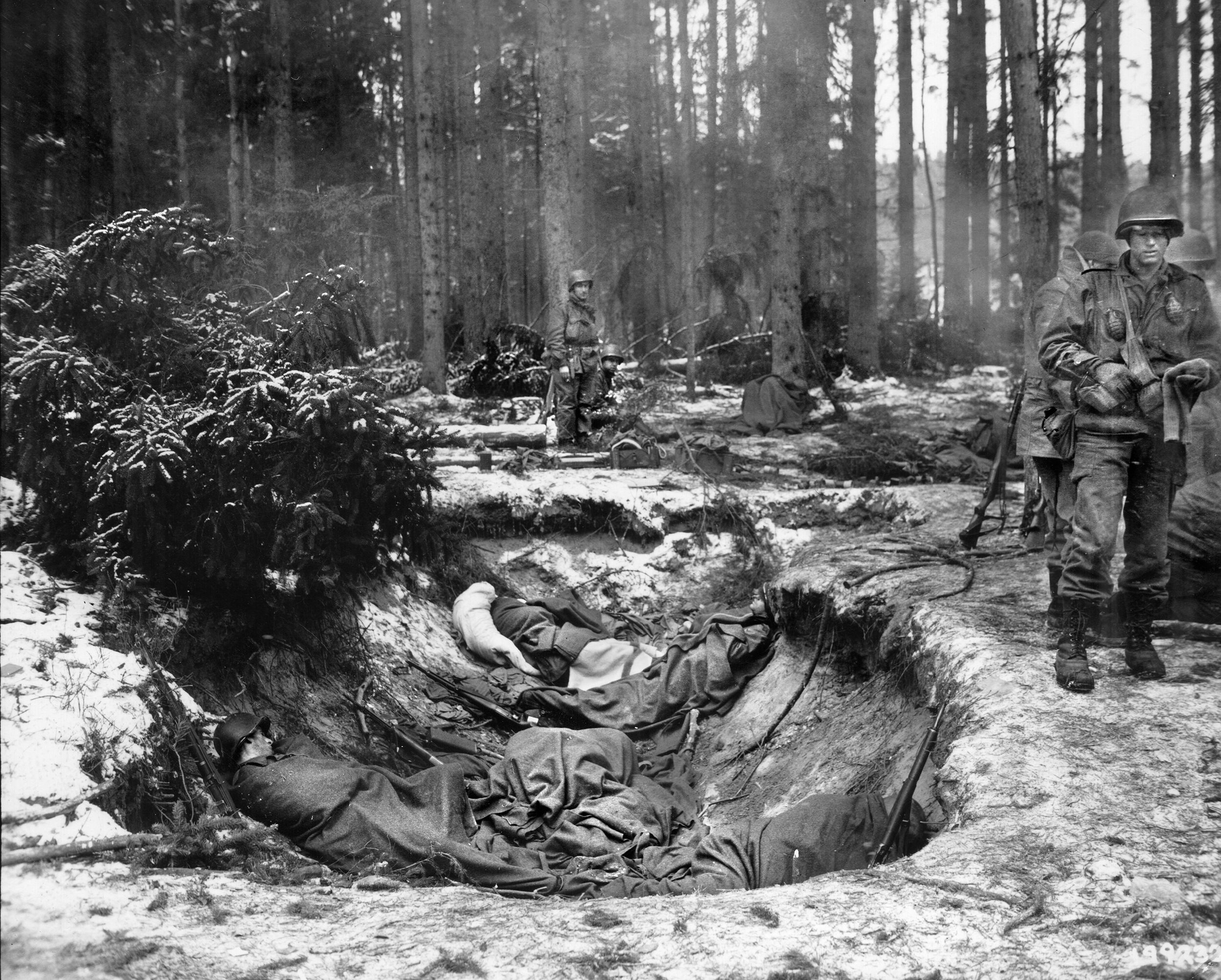 Wrapped in blankets and temporarily placed in a shell hole for cover, these G.I.s of the 274th Infantry Regiment await treatment at an aid station near the front lines after being wounded in the fight with SS troops at Wingen, Germany.