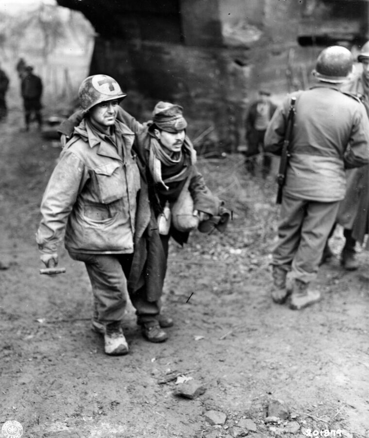 Medic T/5 Max Freeman of the medical detachment, 274th Infantry Regiment, helps a wounded man to safety. The victim was among a group of Eastern European slave laborers who escaped from the Germans during the American attack on the town of Stiring-Wendel, France. He was shot when the Germans opened fire on the fleeing laborers.