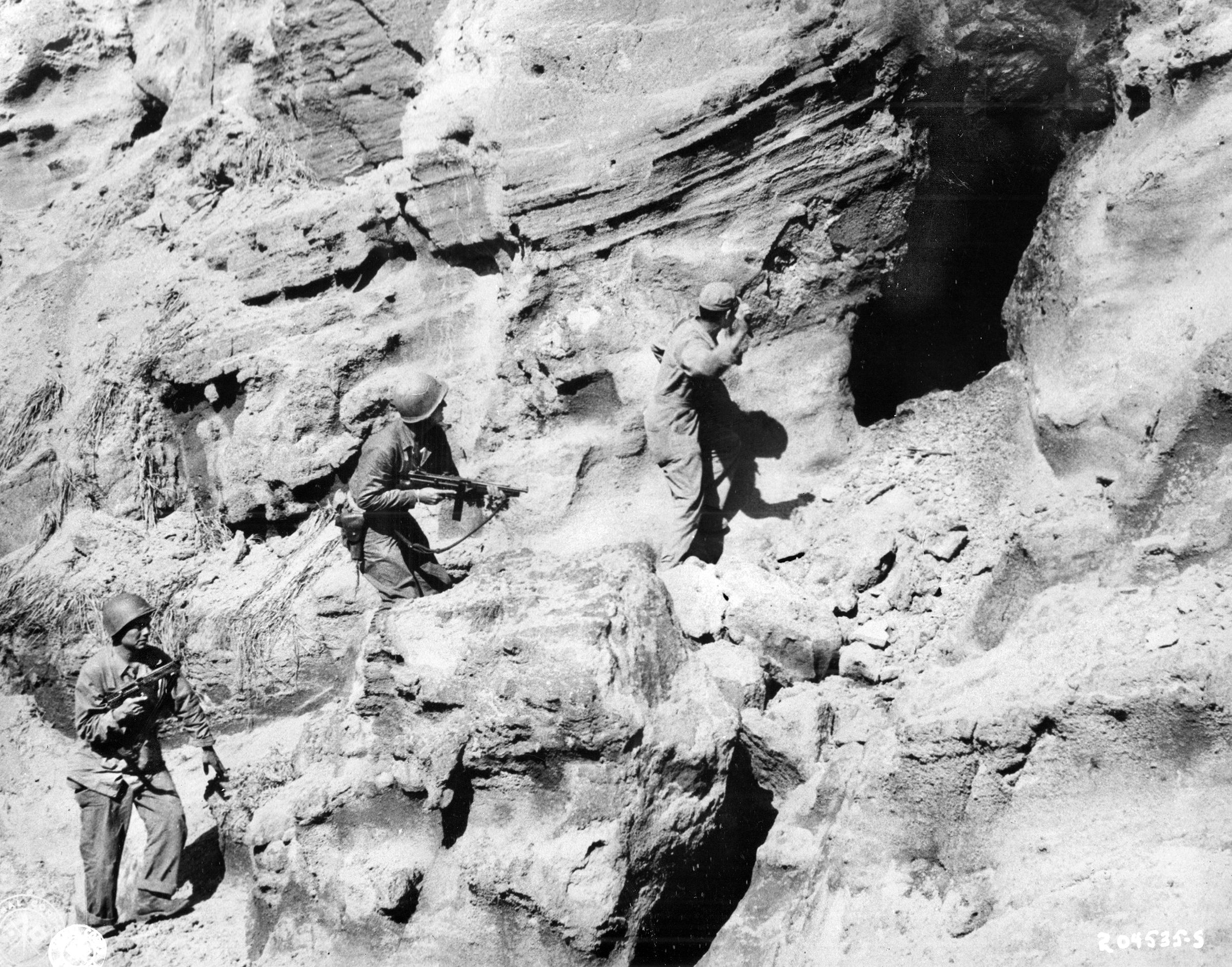 Following a blast by a flamethrower (opposite page), one of the 147th Infantry Regiment’s “Cave Men”prepares to throw a hand grenade into the cave mouth to silence Japanese resistance.