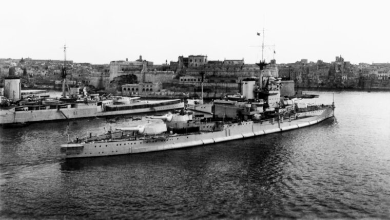 Following an extensive modernization, the battleship HMS Warspite sails past the battlecruiser HMS Hood at Grand Harbor, Valletta, Malta, in 1938. The tiny Mediterranean island became a bastion of British resistance to the Nazis during World War II as aircraft and submarines attacked German supply convoys bound for North Africa. However, the Maltese endured heavy bombing and reached the brink of starvation in the process.