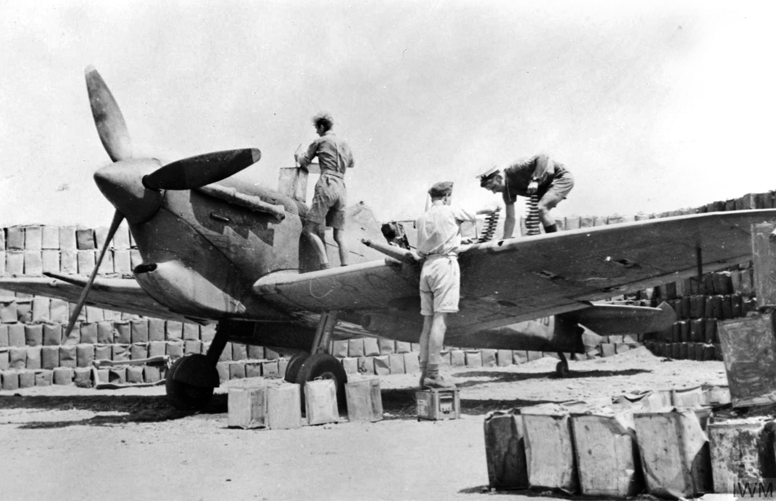 A ground crew services a Supermarine Spitfire V fighter of No. 603 Squadron RAF in a revetment of sand-filled empty fuel cans at Ta Kali, Malta. A British soldier and sailor pitch in to assist with the refueling and rearming of the aircraft. 