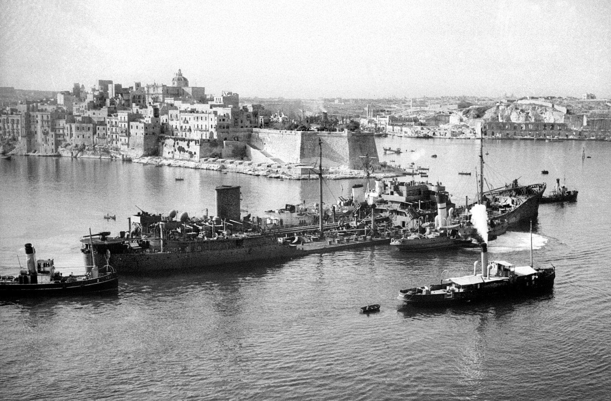 Lashed to the destroyers HMS Penn and HMS Ledbury, the British-flagged tanker Ohio makes port at Grand Harbor, Malta, on August 15, 1942. Ohio was one of five supply ships from an original complement of 14 that comprised the Pedestal convoy. Pedestal was ravaged by Axis attacks en route to Malta, but enough supplies reached port to sustain the garrison and civilian population.