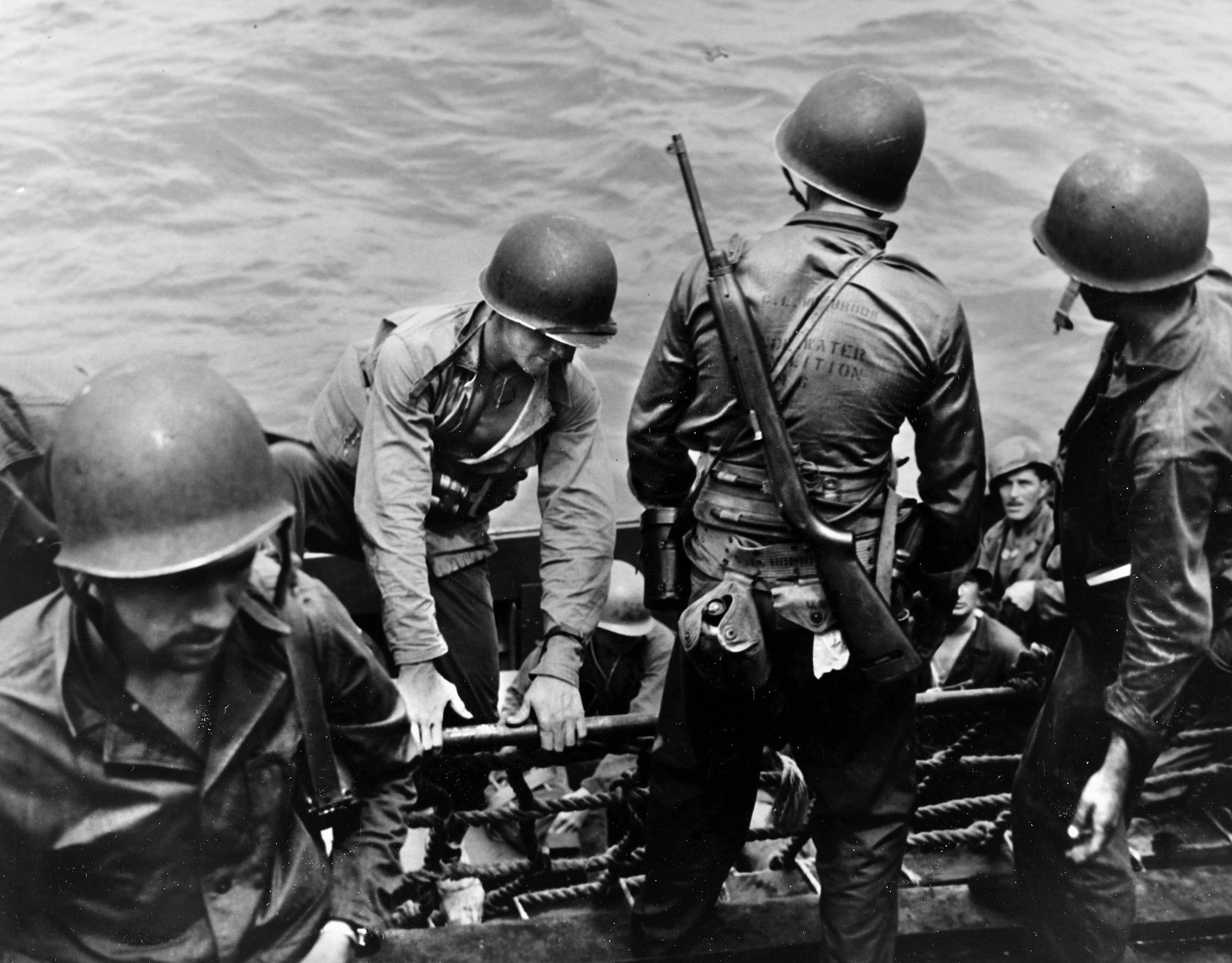 Members of UDT-6 climb aboard a landing craft off the island of Saipan in the Marianas. One of the lightly equipped Navy divers has an M-1 carbine slung over his shoulder, and each of the men wears the life belt that holds their knife and other equipment. 