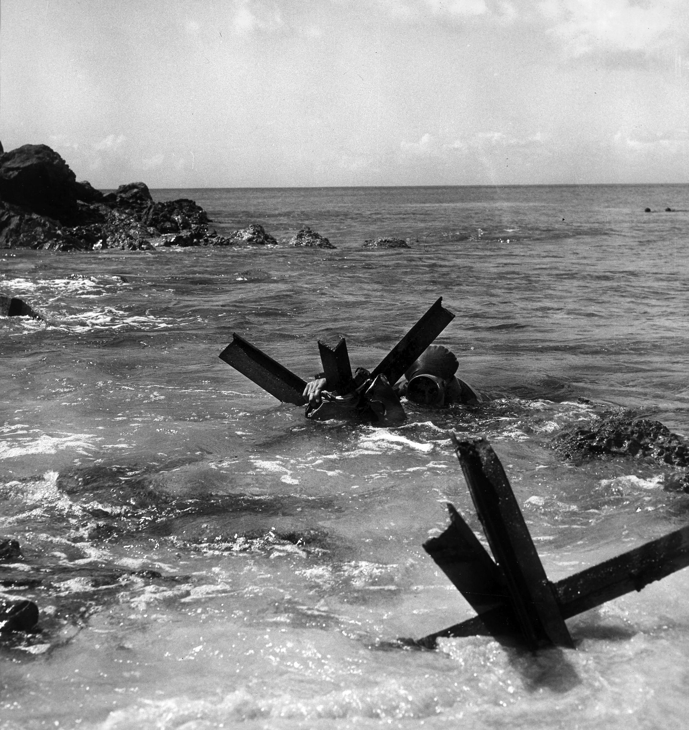 A member of UDT-2 places an explosive charge to destroy a beach obstacle during assault training at Little Creek, Virginia. The Little Creek facility was established in 1942 and remains the primary base for the amphibious forces of the U.S. Navy’s Atlantic Fleet. 