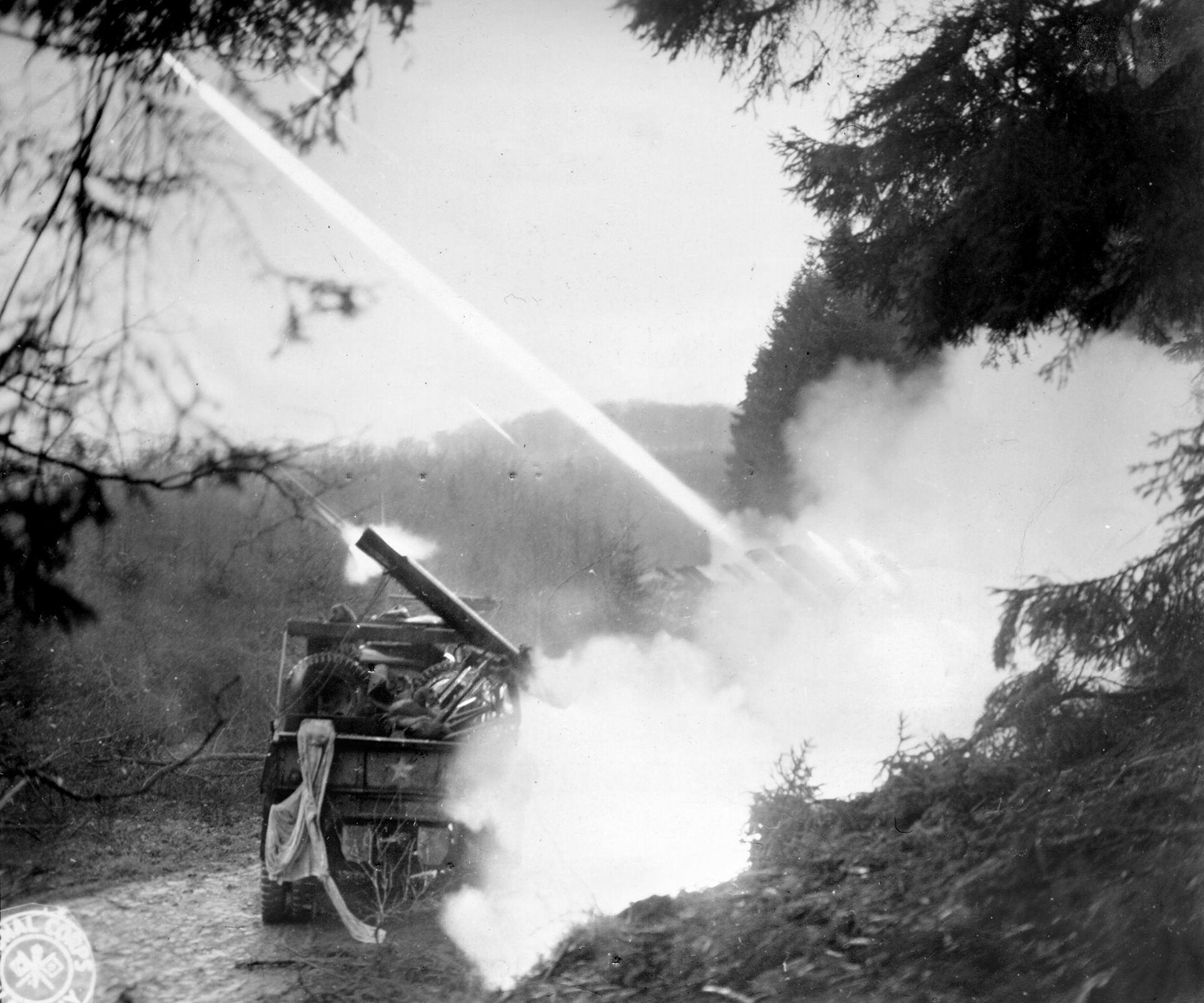 GIs of 18th Field Artillery Battalion use 4.5-inch rockets fired from two-and-a-half-ton trucks to dislodge German defenders. Tree bursts were especially deadly for Americans and Germans alike.