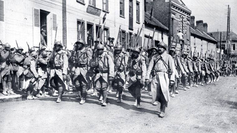 African Senegalese soldiers marching down a street in a town in France during World War I.